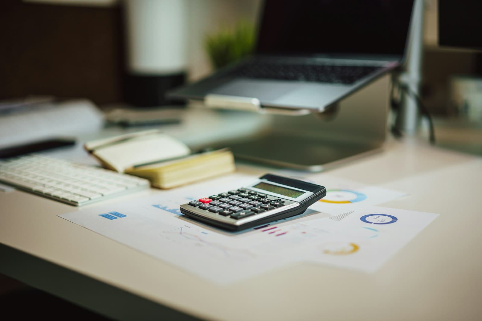 Calculator resting on financial charts beside a laptop