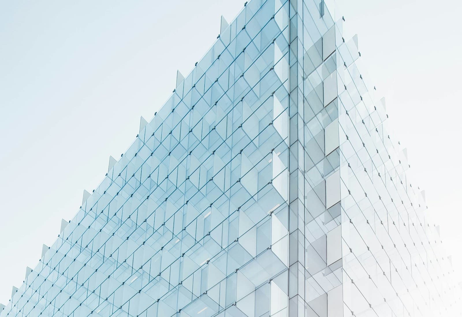Angular glass building façade viewed from below against a pale blue sky.
