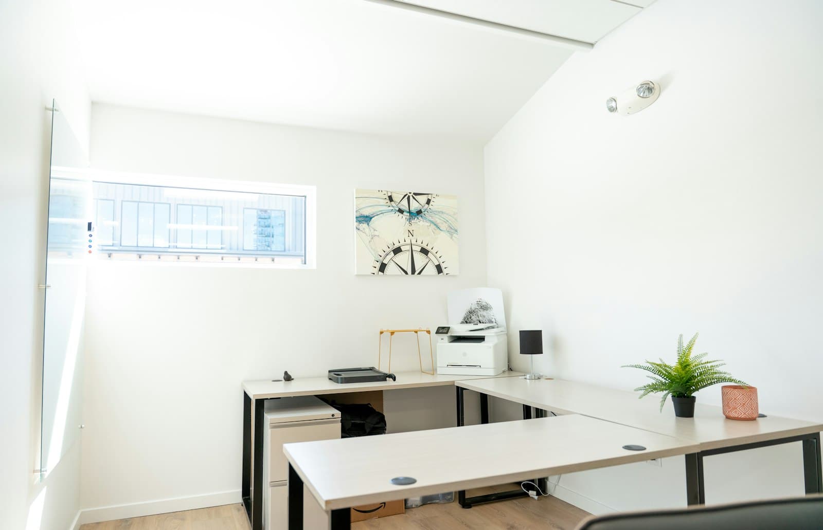 Bright unoccupied office with desks, a printer and a window