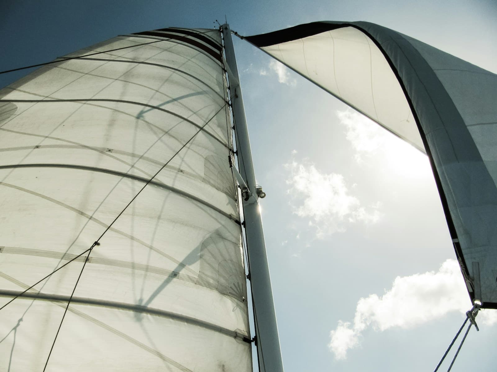 White sailboat sails and rigging viewed from below against a blue sky.