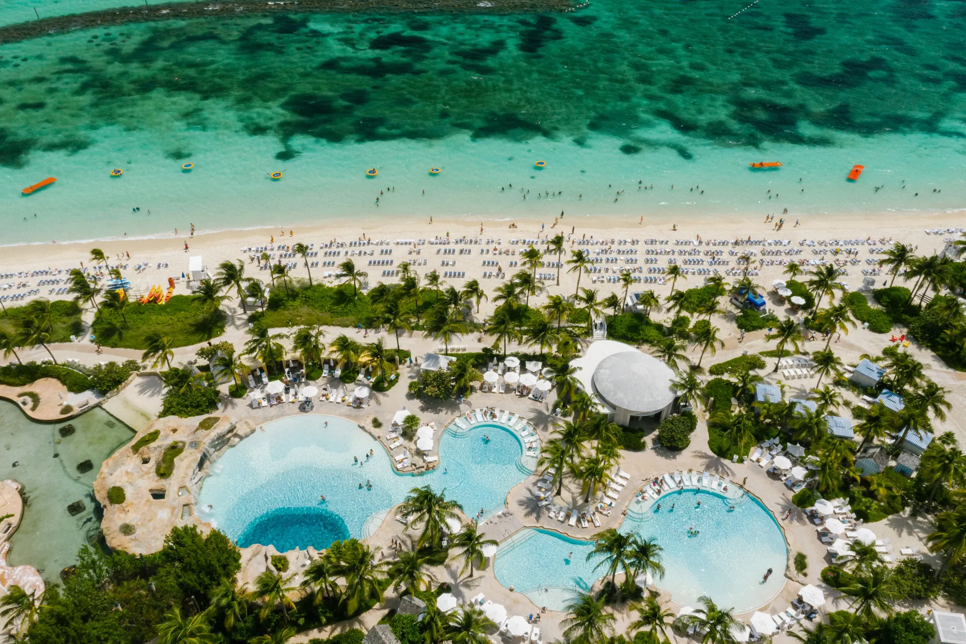 Aerial view of resort swimming pools, palm trees and a sandy Caribbean shoreline