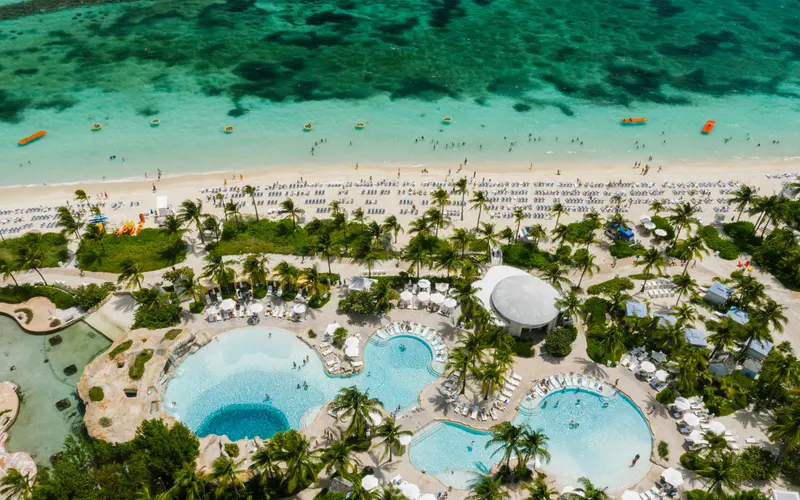 Aerial view of resort swimming pools, palm trees and a sandy Caribbean shoreline