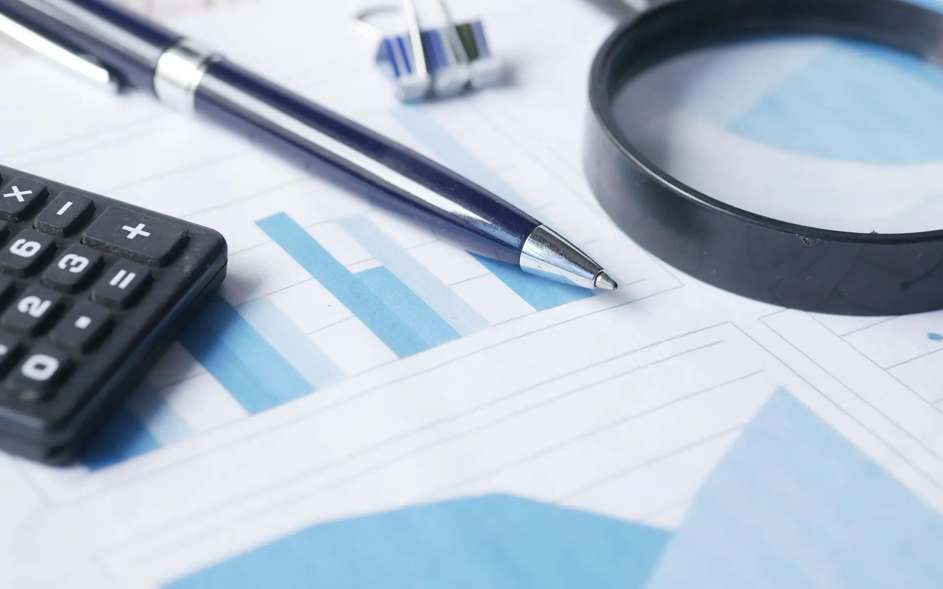 Magnifying glass, calculator and pen on financial charts.