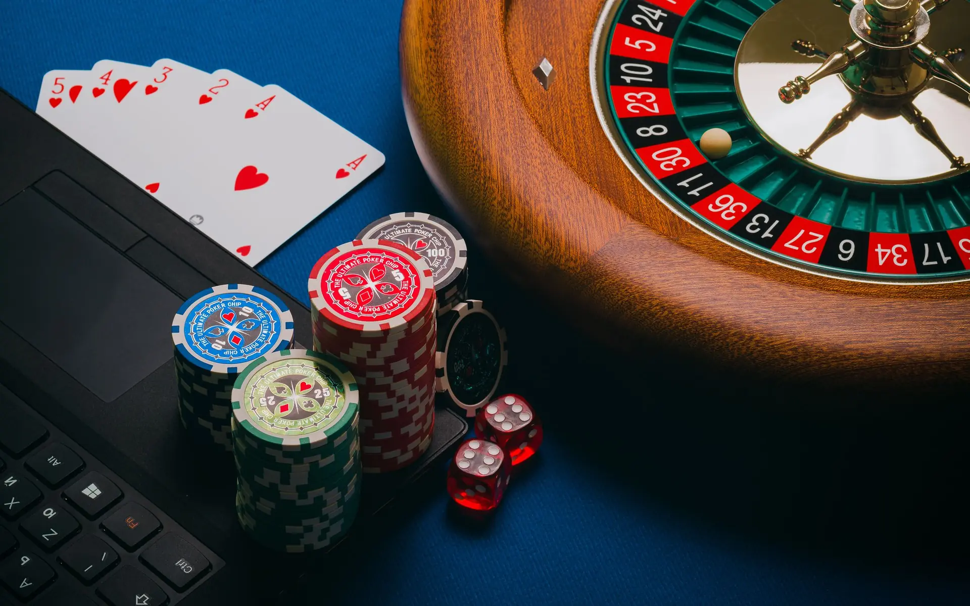 Roulette wheel, playing cards and casino chips beside a laptop.